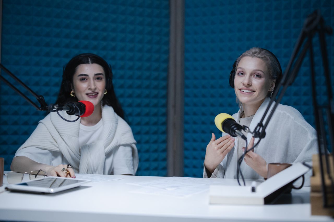 services-02 Two women podcasters engaging in discussion inside a modern recording studio with microphones.
